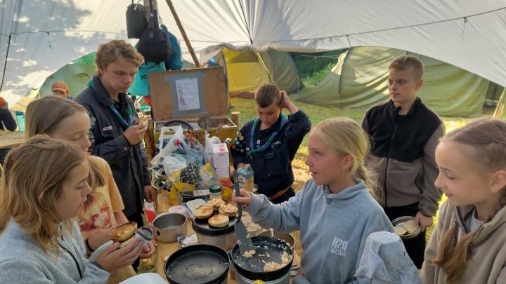 Stjernetelt med lejrkøkken og spejdere der spiser morgenmad